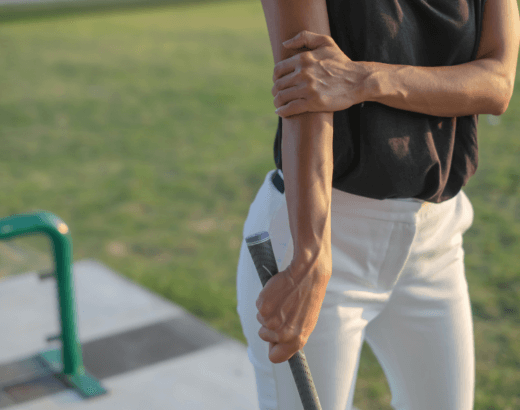 A person holds their outer elbow in pain while playing golf.