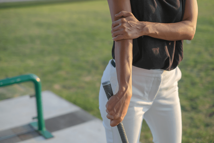 A person holds their outer elbow in pain while playing golf.
